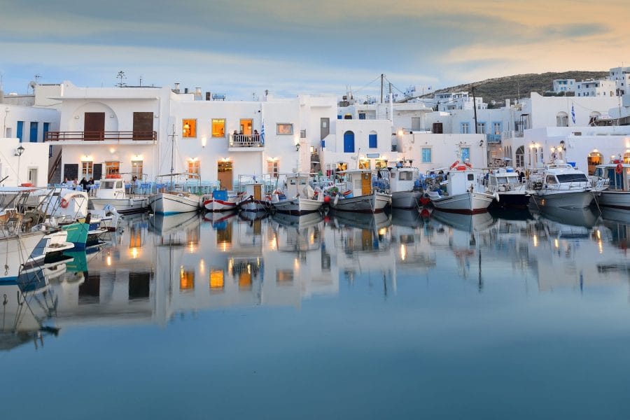 Το λιμάνι της Νάουσας στην Πάρο το σούρουπο, με καΐκια δεμένα και τα λευκά σπίτια να καθρεφτίζονται στο νερό